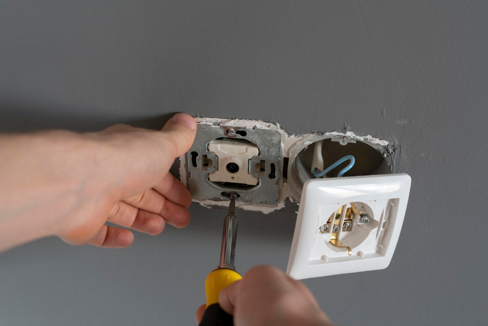 Technicien effectuant le remplacement d’une prise électrique encastrée, avec démontage du mécanisme, câblage visible et raccordement des conducteurs
